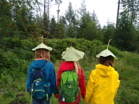 Drei Kinder stehen im Reden und nutzen große Blätter, um nicht nass zu werden